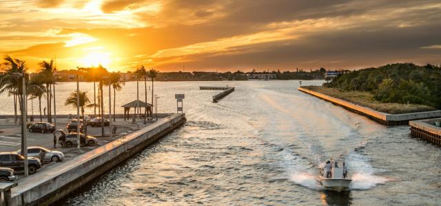 small yacht cruising along florid waters beside the palm trees full parking lot during sunset